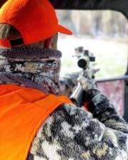 A hunter with gear and bow walks on hunting land.
