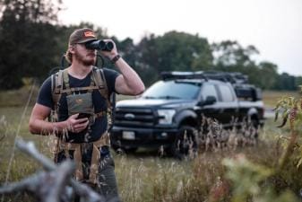 A hunter uses binoculars when scouting for deer.