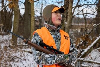 Hunter in blaze orange with rifle, best caliber for small game concept.