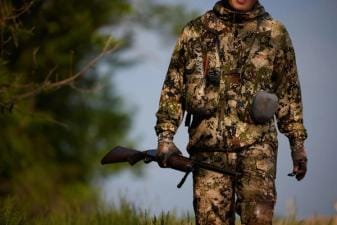 A hunter in camo holding a rifle in the field, get a Mississippi hunting license concept.