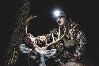 A hunter wearing a head lamp holds up a deer's antlers and head after a hunt, HuntWise app concept.