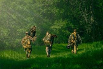 Three hunters from Blueline Bowhunters walking, one carries a turkey, turkey hunting tips concept.