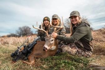Three women in camo pose with a deer after a kill, find the best hunting time with HuntCast concept.