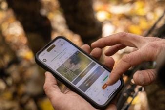 Close-up of a hunter's hands holding a phone and using the HuntWise hunting app.