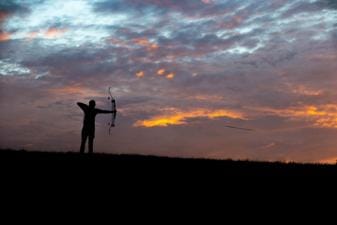 A bowhunter in the distance draws the bow, hunting whitetail deer concept.
