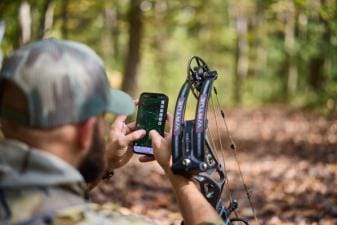 Hunter with bow using phone showing HuntWise on screen, how to use a hunting app concept.