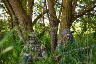 A man and a woman in camo sitting against trees with a shotgun, Osceola turkey hunt concept.