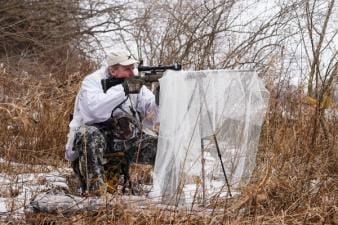 A hunter using a stand in the brush for coyote hunting.