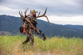 A hunter walks on a ridge carrying a large set of antlers, HuntWise pros concept.