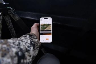 Hunter's hand holding a phone showing HuntCast in the HuntWise app.