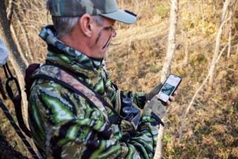 A hunter looks at a phone in the field, best wind direction app for hunting concept.