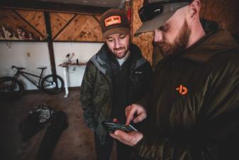 Two hunters looking at a phone, share nearby hunt areas concept.