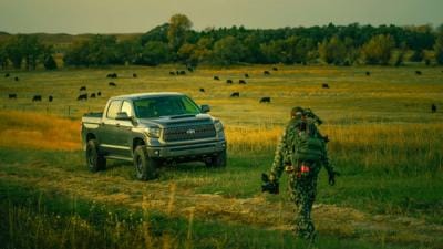 Hunter with gear walks toward truck in a field, leave no trace hunting concept.