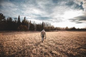 A hunter walks across a field with hunting gear, understanding deer movement concept.