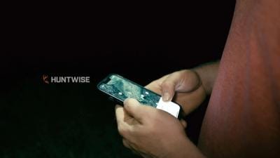 Close-up of hands holding phone showing hunting app with HuntWise logo.