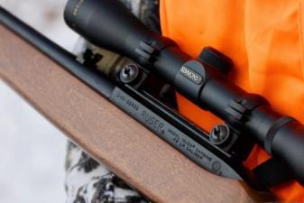 Close-up of hunter's orange vest and small game rifle, rabbit hunting gear list concept.