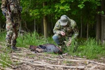 A hunter kneels next to a turkey kill, where to shoot a turkey concept.