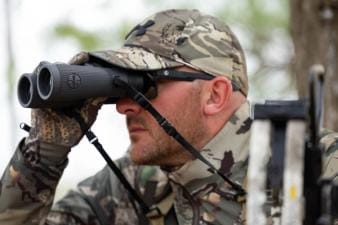 A hunter in camo uses binoculars, choosing lightweight hunting clothes concept.
