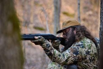 Ben Cole of RootedTV aims a shotgun in the woods, spring hunting concept.