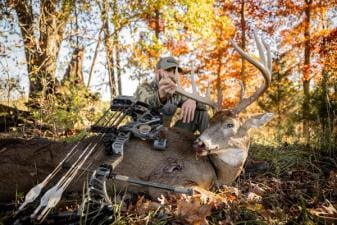 Hunter with buck deer and bow after hunt, represents post season bow maintenance.