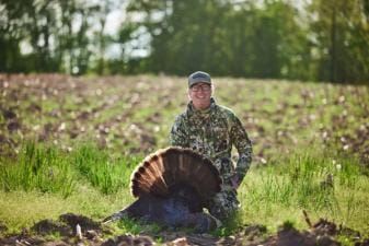 A hunter smiles and poses with a turkey after a successful hunt.