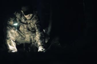 A hunter in camo with a flashlight in the dark, coyote hunting at night concept.