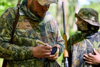 Hunter using turkey call with boy, best turkey hunting gear concept.