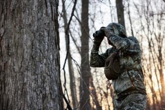 Hunter using binoculars in the woods to scout, turkey scouting concept.