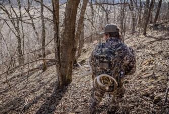 A hunter in the woods wearing a pack with shed antlers attached.