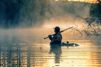A hunter in the water with a shotgun and waterfowl decoys, best decoys concept.